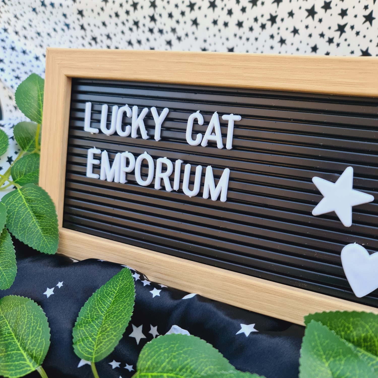 An eye-catching pegboard showcasing 'Lucky Cat Emporium' in bold lettering, accompanied by a heart and a star, set against a whimsical background adorned with twinkling stars and lush green leaves, reflecting the store's vibrant and enchanting character.