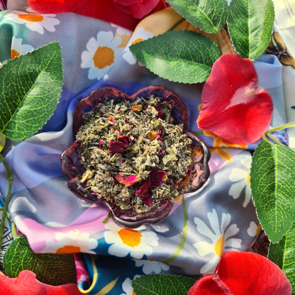 A captivating image of The Dreamy Blend in an pink flower shaped glass bowl, featuring a mixture of green raspberry leaf and mugwort, beautifully accented with specks of rose petals and lavender.