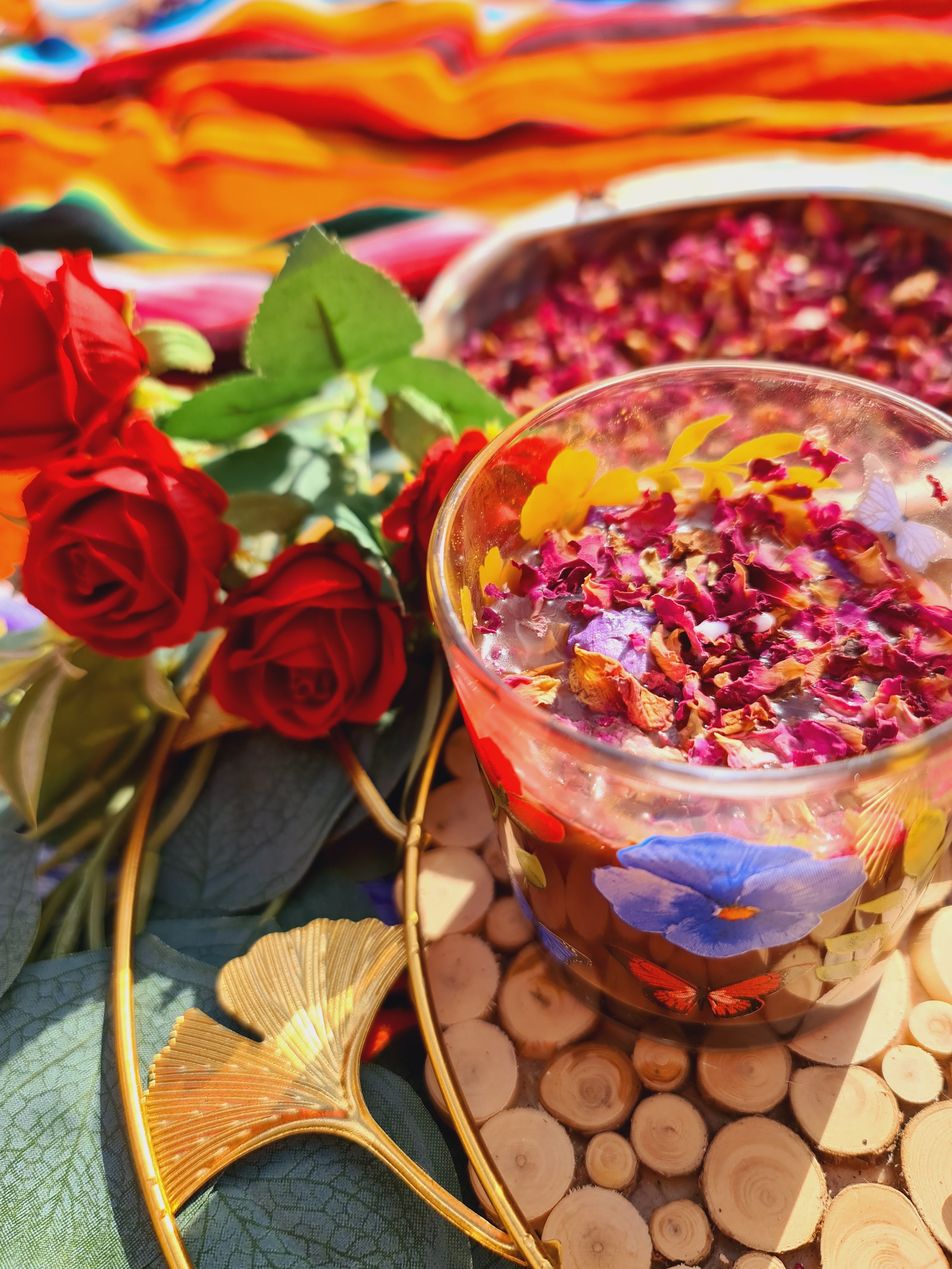 An exquisite image of a blue lotus and rose petal cacao drink, served in a charming floral glass, garnished with edible dried rose petals. A picturesque abalone shell filled with rose petals and fresh roses in the background adds to the visual delight and elegance..